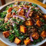 A close-up of a hearty sweet potato kale salad with quinoa, red onion, and pumpkin seeds.
