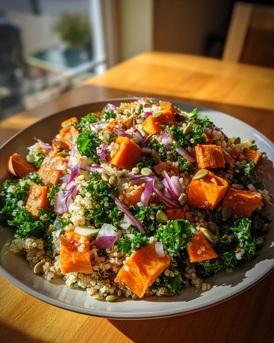 A vibrant and hearty sweet potato kale salad with quinoa, red onion, and pumpkin seeds, served on a plate.