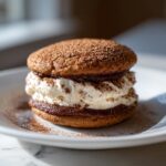 A close-up of a delicious tiramisu cookie sandwich filled with creamy mascarpone and dusted with cocoa powder.