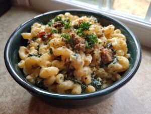 A bowl of creamy Tuscan mac and cheese topped with crumbled sausage, spinach, and fresh parsley.