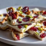 A stack of broken pieces of white chocolate pretzel bark, topped with dried cranberries and pistachios.