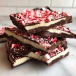 A stack of rich, layered peppermint bark squares topped with crushed candy canes.