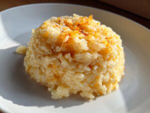 A perfectly molded serving of creamy, cheesy rice topped with browned cheese on a white plate.