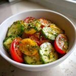 Close-up of a fresh cucumber tomato salad featuring sliced red and yellow tomatoes and cucumbers tossed in a light vinaigrette with dill.
