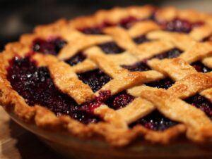 Close-up of a freshly baked blackberry pie featuring a golden brown lattice crust over bubbling dark purple filling.
