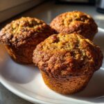 Close-up of three perfectly baked, golden brown bran muffins sitting on a white plate.