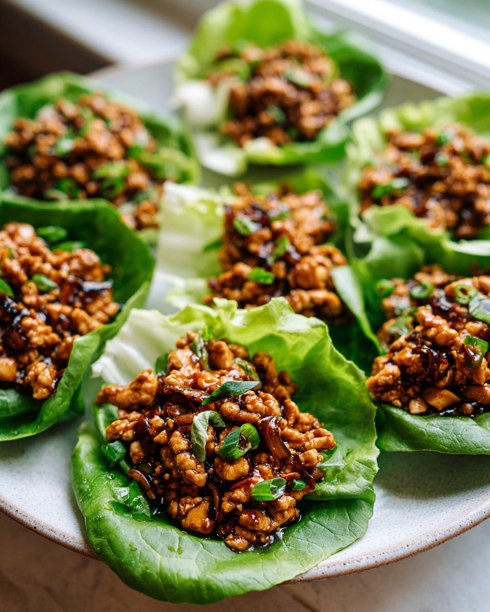 Close-up of several servings of savory chicken lettuce wraps garnished with green onions on a light plate.