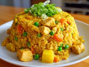 A mound of vibrant yellow pineapple fried rice mixed with chicken, peas, and carrots, topped with green onions.
