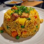 A perfectly molded serving of golden yellow pineapple fried rice topped with crispy pork pieces and green onions.