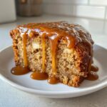 Close-up of a moist slice of apple cake topped generously with dripping caramel sauce.