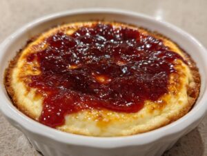 Close-up of a baked pepper jelly cheese dip, featuring melted cheese topped with glistening red pepper jelly in a white ramekin.