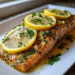 Close-up of a perfectly baked salmon recipe fillet topped with lemon slices and fresh parsley.