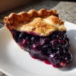 Close-up of a juicy slice of homemade blueberry pie recipe with a flaky golden crust.