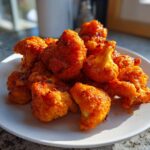 Close-up of crispy, bright orange buffalo cauliflower florets piled on a white plate.