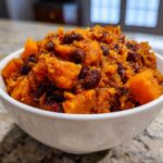 Close-up of a white bowl filled with chunky, orange butternut squash chili mixed with dark red beans.