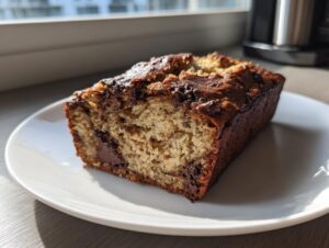 A thick slice of moist peanut butter banana bread with melted chocolate chips on a white plate.