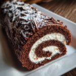 Close-up of a slice of chocolate yule log cake showing the rich dark sponge rolled with white cream filling.