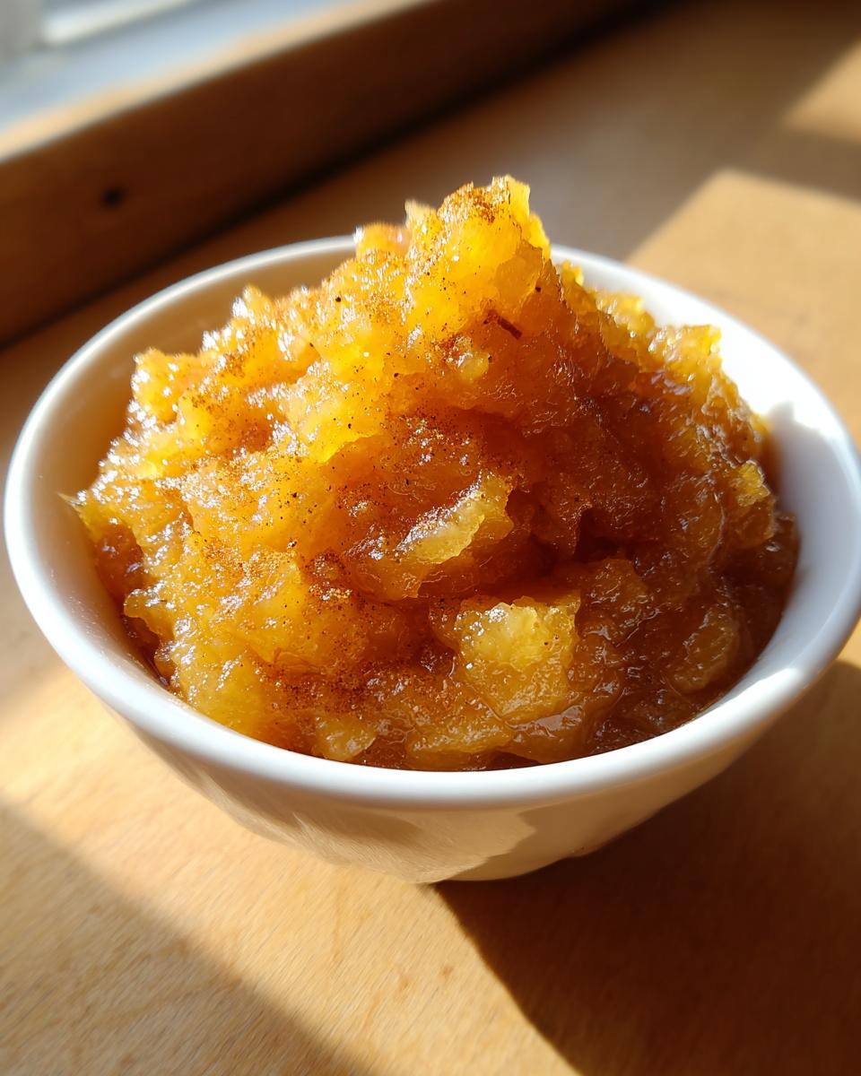 Close-up of chunky, golden-brown homemade applesauce sprinkled with cinnamon in a small white bowl.