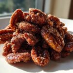 A close-up pile of glistening cinnamon sugar pecans coated in sparkling sugar crystals, sitting on a white plate.