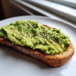 Close-up of mashed avocado toast topped with black pepper and everything bagel seasoning.