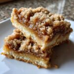 Two stacked, gooey apple pie bars with a crumb topping served on a white plate.