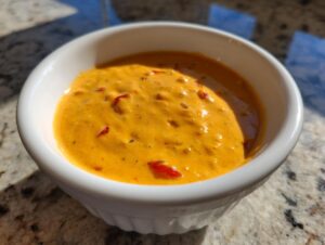 Close-up of vibrant orange cottage cheese queso with visible red pepper pieces in a small white bowl.