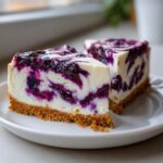 Two slices of creamy no-bake blueberry cheesecake with a graham cracker crust on a white plate.