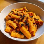 Close-up of rigatoni pasta coated in a creamy orange butternut squash pasta sauce, topped with crispy sage leaves.