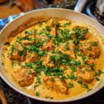 Pieces of seasoned cajun chicken simmering in a rich, creamy sauce, topped generously with fresh parsley.