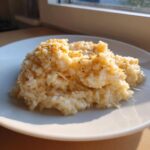A close-up of creamy, cheesy rice served on a white plate, showing melted cheese strings.