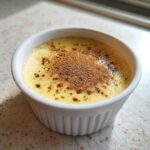 A creamy, yellow egg custard topped with a dusting of brown spice, served in a white fluted ramekin.