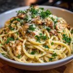 Close-up of creamy pasta tossed in a rich garlic parmesan sauce, topped with grilled chicken pieces and fresh parsley.