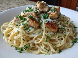 Close-up of creamy pasta coated in sauce, topped with seared chicken pieces, grated parmesan, and fresh parsley for a garlic parmesan dish.
