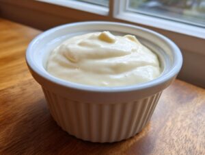 A close-up of thick, creamy homemade garlic sauce served in a small, white, fluted ramekin.