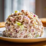 A mound of creamy ham salad mixed with diced ham, green celery, and red onion served on a white plate.