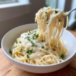 A fork lifting spaghetti coated in creamy sauce, showing a dramatic cheese pull from a bowl of parmesan pasta.