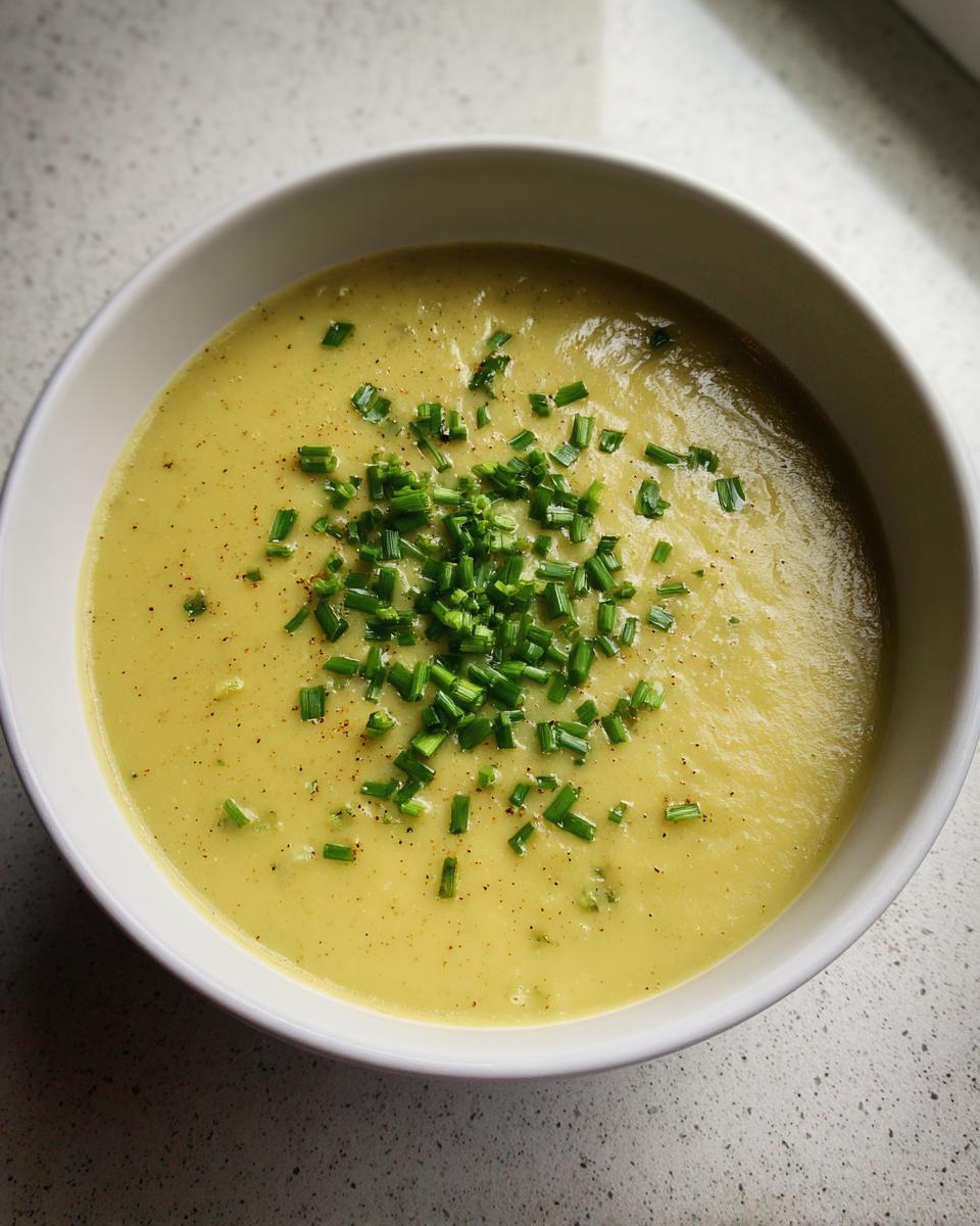 A close-up overhead view of a bowl of creamy potato leek soup, garnished generously with fresh chopped chives.