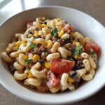Close-up of creamy taco pasta salad with elbow macaroni, ground beef, corn, black beans, and tomatoes in a white bowl.