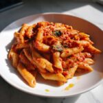 A white bowl filled with creamy tomato basil pasta featuring penne noodles coated in a rich red sauce and fresh basil.
