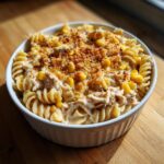 A close-up of creamy tuna pasta made with fusilli, corn, and a crispy breadcrumb topping, served in a white ramekin.