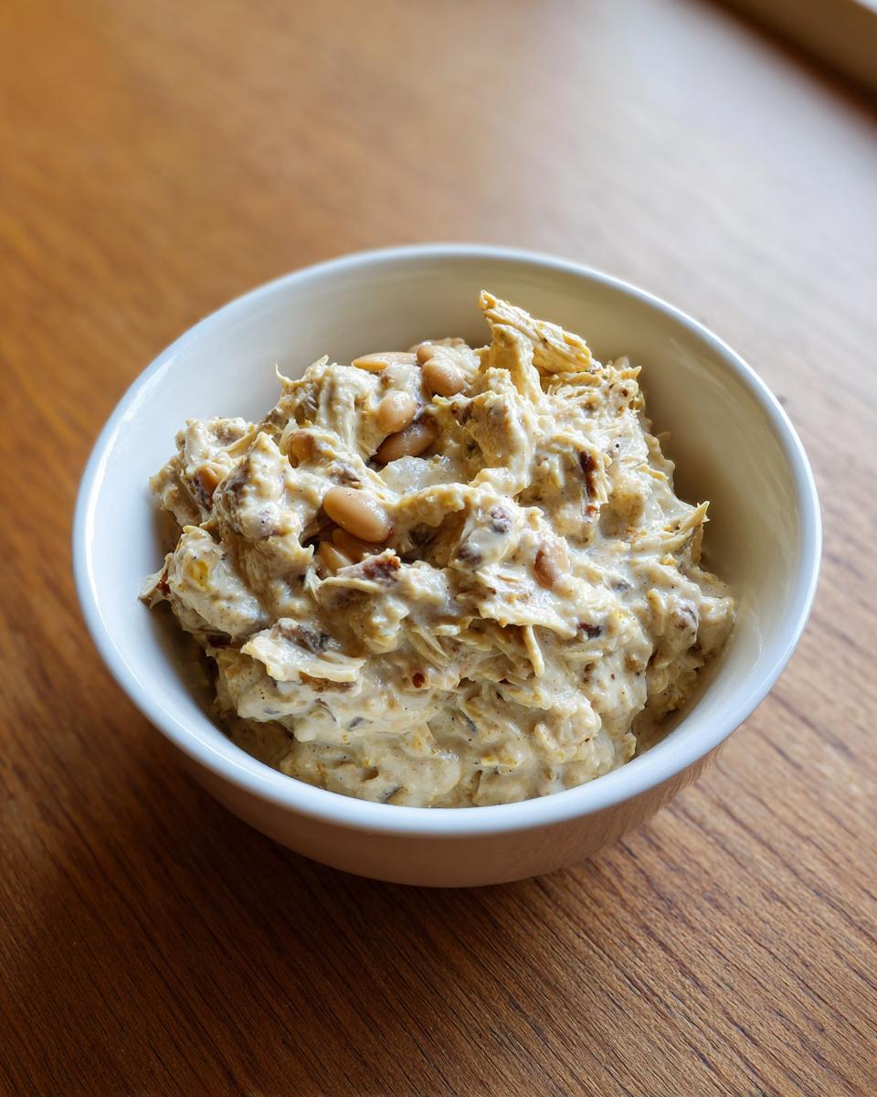A close-up of creamy white chicken chili with beans served in a small white bowl on a wooden table.