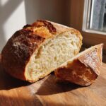 A freshly baked Italian bread loaf, sliced open to show the airy interior and golden crust, resting on a wooden board.