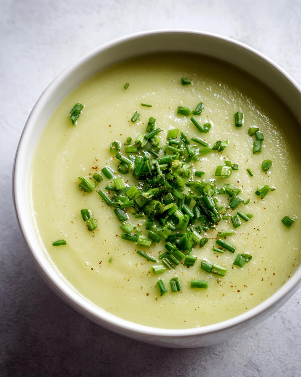 Overhead close-up of creamy potato leek soup in a white bowl, garnished generously with fresh chopped chives.