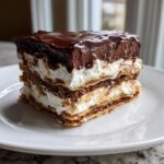 A decadent slice of eclair cake showing layers of flaky pastry, white cream filling, and rich chocolate topping.