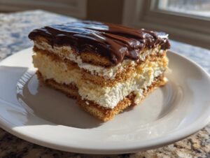 A decadent slice of eclair cake featuring layers of graham crackers, vanilla cream filling, and rich chocolate glaze.