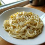 Close-up of fettuccine pasta coated in rich homemade alfredo sauce and topped with cracked black pepper.
