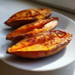 Three halves of perfectly baked sweet potatoes, split open to show the bright orange, fluffy interior.