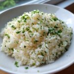 A close-up of fluffy white butter rice generously topped with finely chopped green parsley in a white bowl.