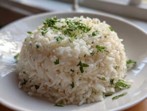 A mound of fluffy white butter rice garnished generously with chopped fresh green parsley on a white plate.