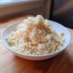 A close-up of fluffy cauliflower rice piled high in a white bowl on a wooden surface.